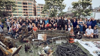 A large group of cleanup volunteers stand behind a large pile of marine debris