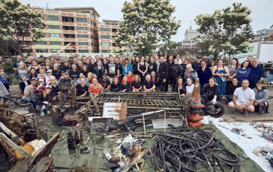 A large group of cleanup volunteers stand behind a large pile of marine debris