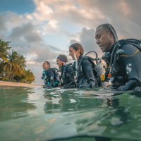 Four divers walking into the water from a beach in Fiji