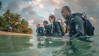Four divers walking into the water from a beach in Fiji