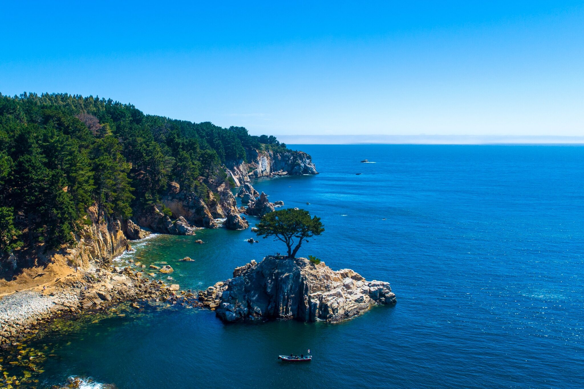 An island with a loan tree along a rugged coastline in Chile with a small boat near the island