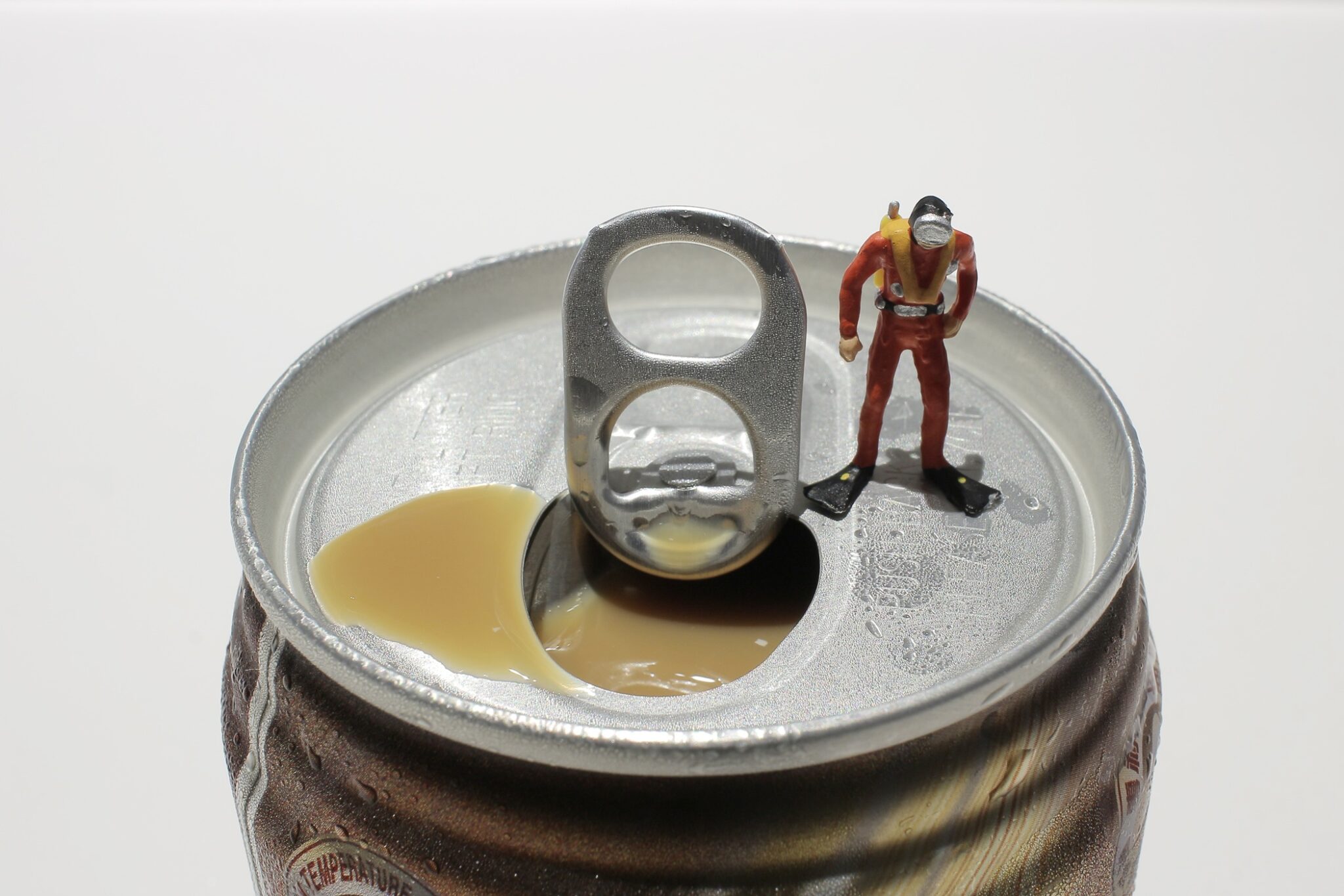 A miniature toy diver stands on top of an open beverage can