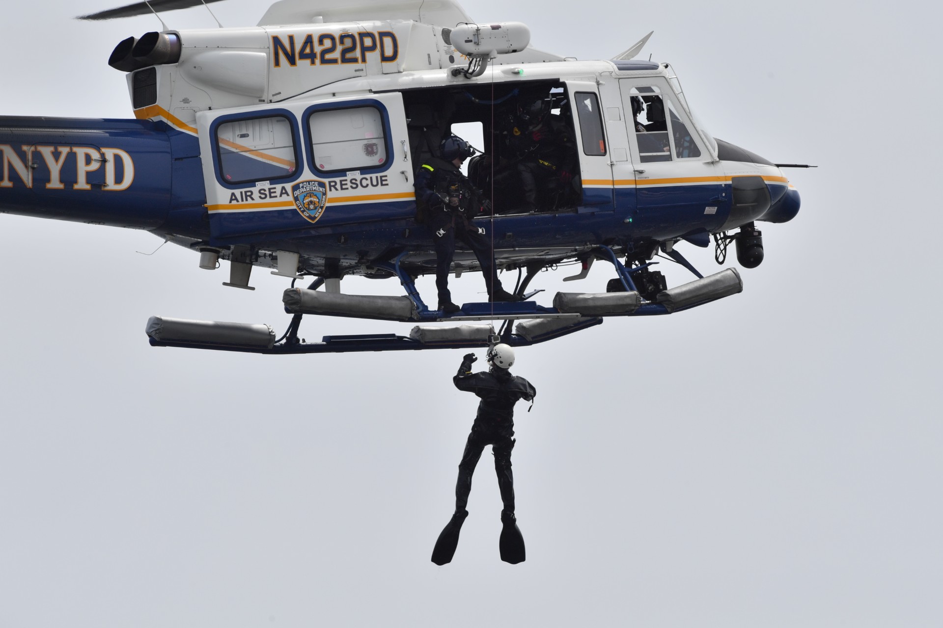 An NYPD Scuba Team member dangles from a Bell helicopter while other dive team members watch from above