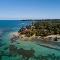 An aerial view of Bocas del Toro in Panama showing clear water and reefs leading up to a sandy beach with a few buildings at the waters' edge