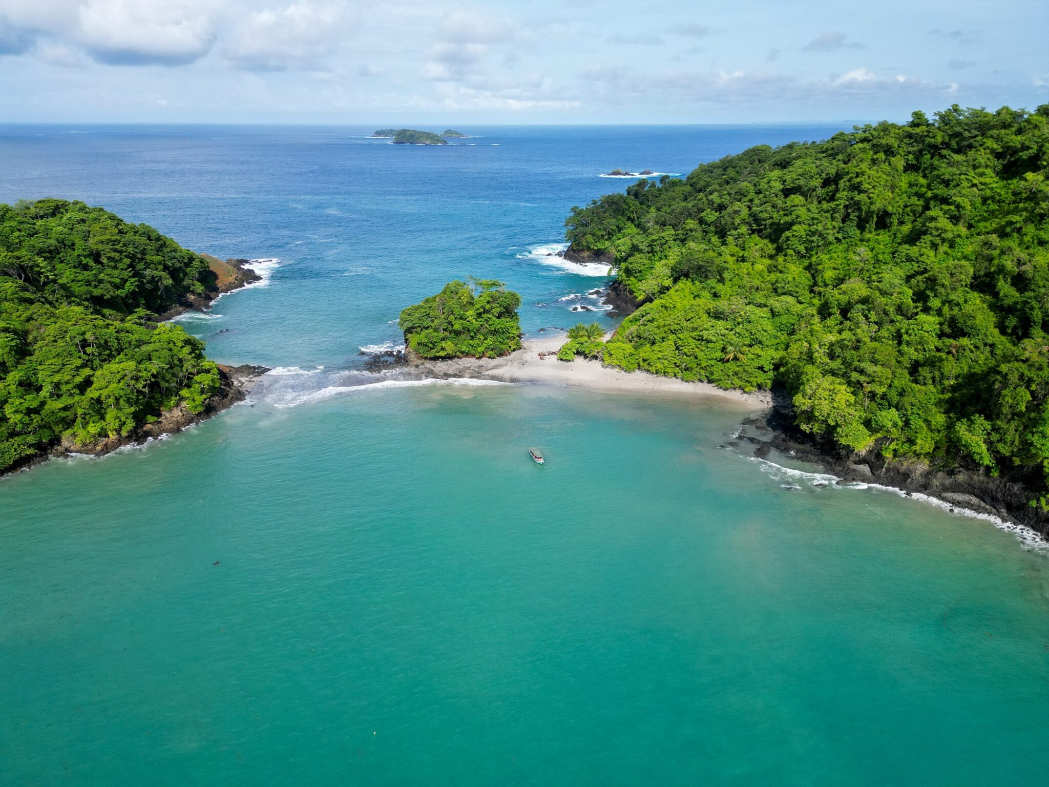 A small sand spit connects two islands covered in green foliage.
