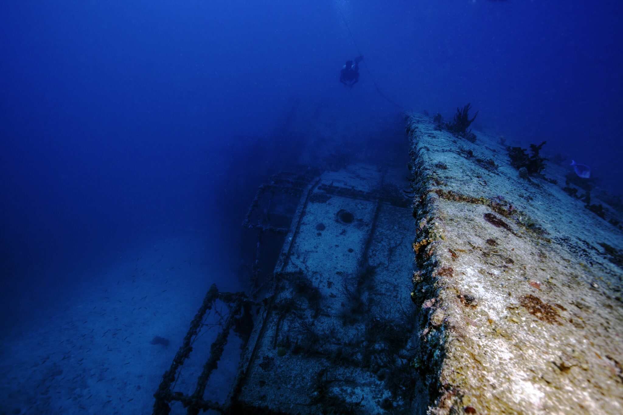 An underwater shipwreck laying on its side in the John Pennekamp State Park in Key Largo, Florida. With a technical diver swimming over it. The USCG Bibb.