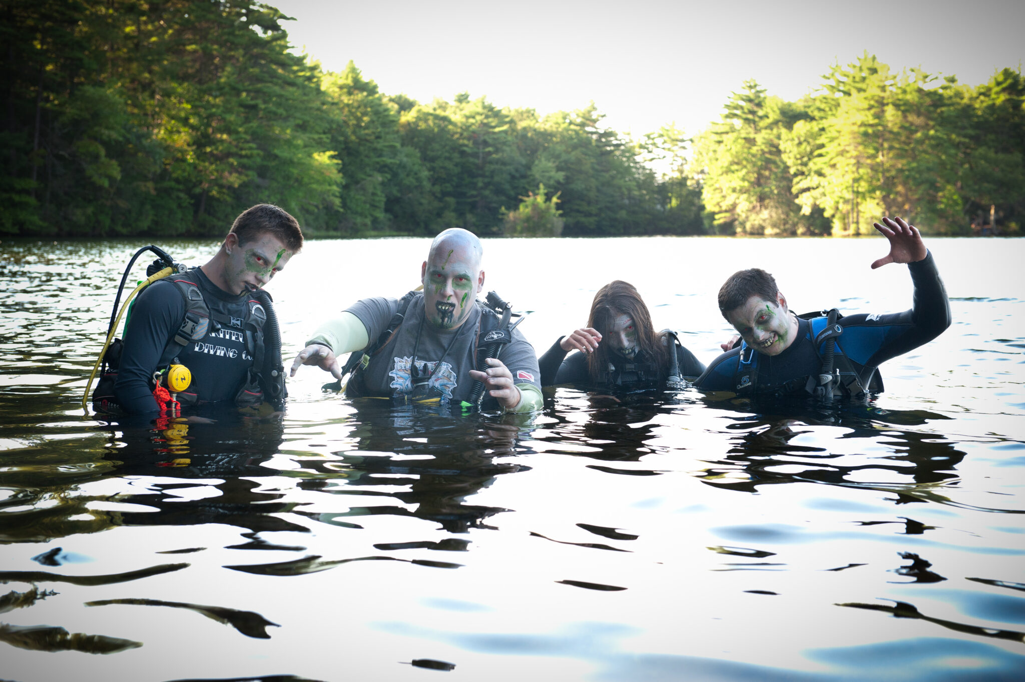 Four scuba divers wearing zombie makeup look menacing in a lake