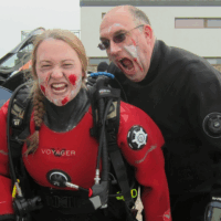 Two divers in zombie makeup, one diver pretends to bite the other