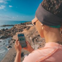 A woman stands on a beach looking at a phone in her hand
