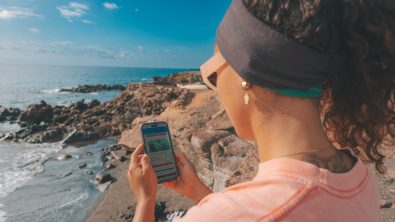 A woman stands on a beach looking at a phone in her hand