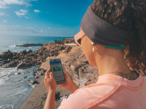 A woman stands on a beach looking at a phone in her hand