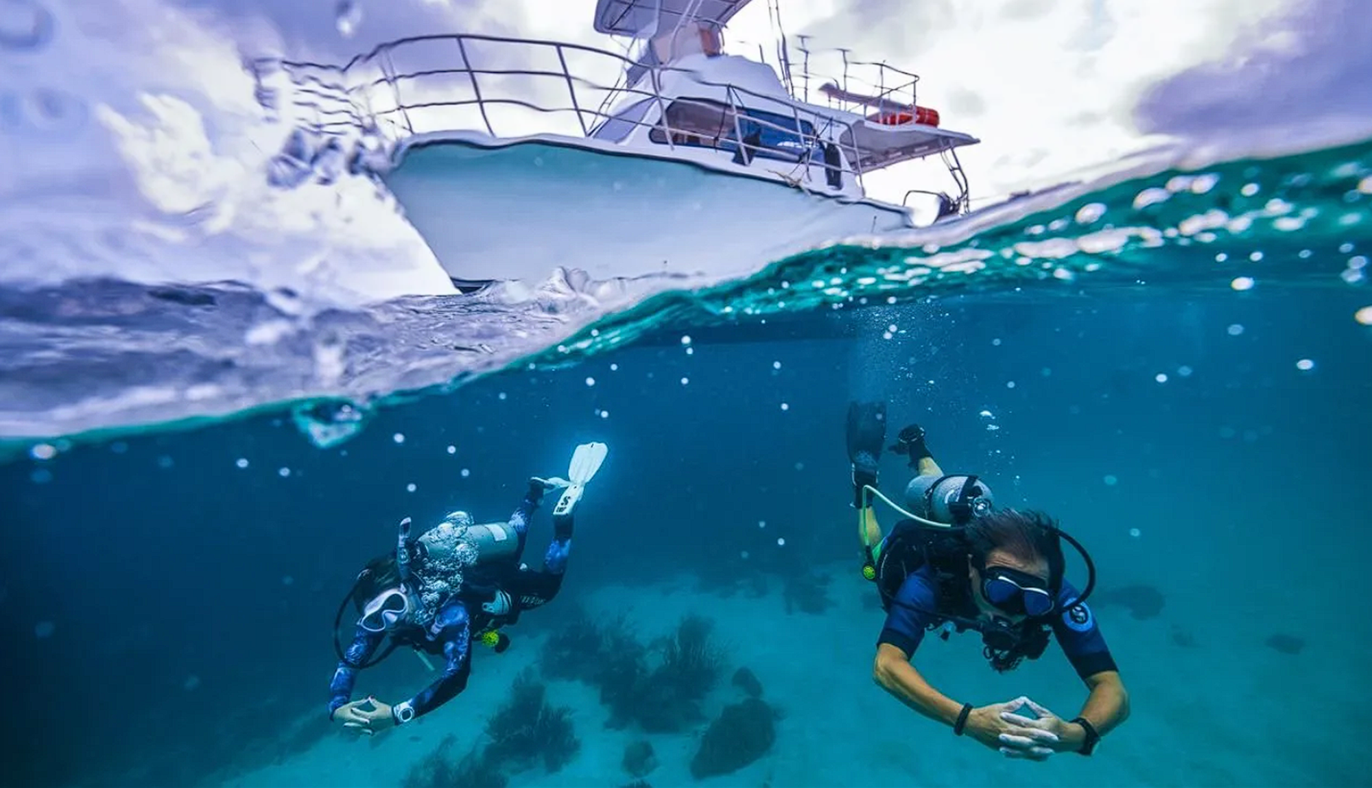 An over under shot of two divers underwater with a small dive boat above them