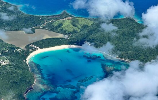 An aerial view of Culebra Island (Isla Culebra) in Puerto Rico. A blue bay and green slopes can be seen beneath a smattering of white cloud.