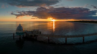 Aerial shot of a diving bell at the end of a pier at sunrise golden hour revealing the rising sun in the Baltic sea, Germany