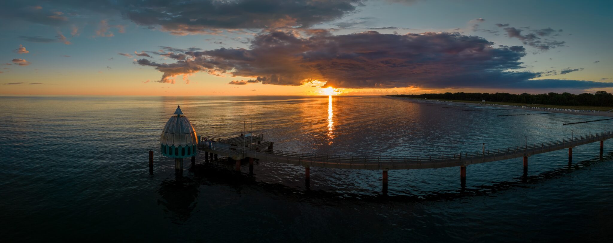 Aerial shot of a diving bell at the end of a pier at sunrise golden hour revealing the rising sun in the Baltic sea, Germany