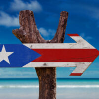 An arrow-shaped Puerto Rican flag on a wooden post with Caribbean blue water in the background