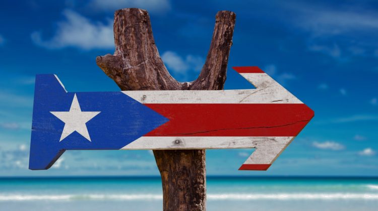 An arrow-shaped Puerto Rican flag on a wooden post with Caribbean blue water in the background