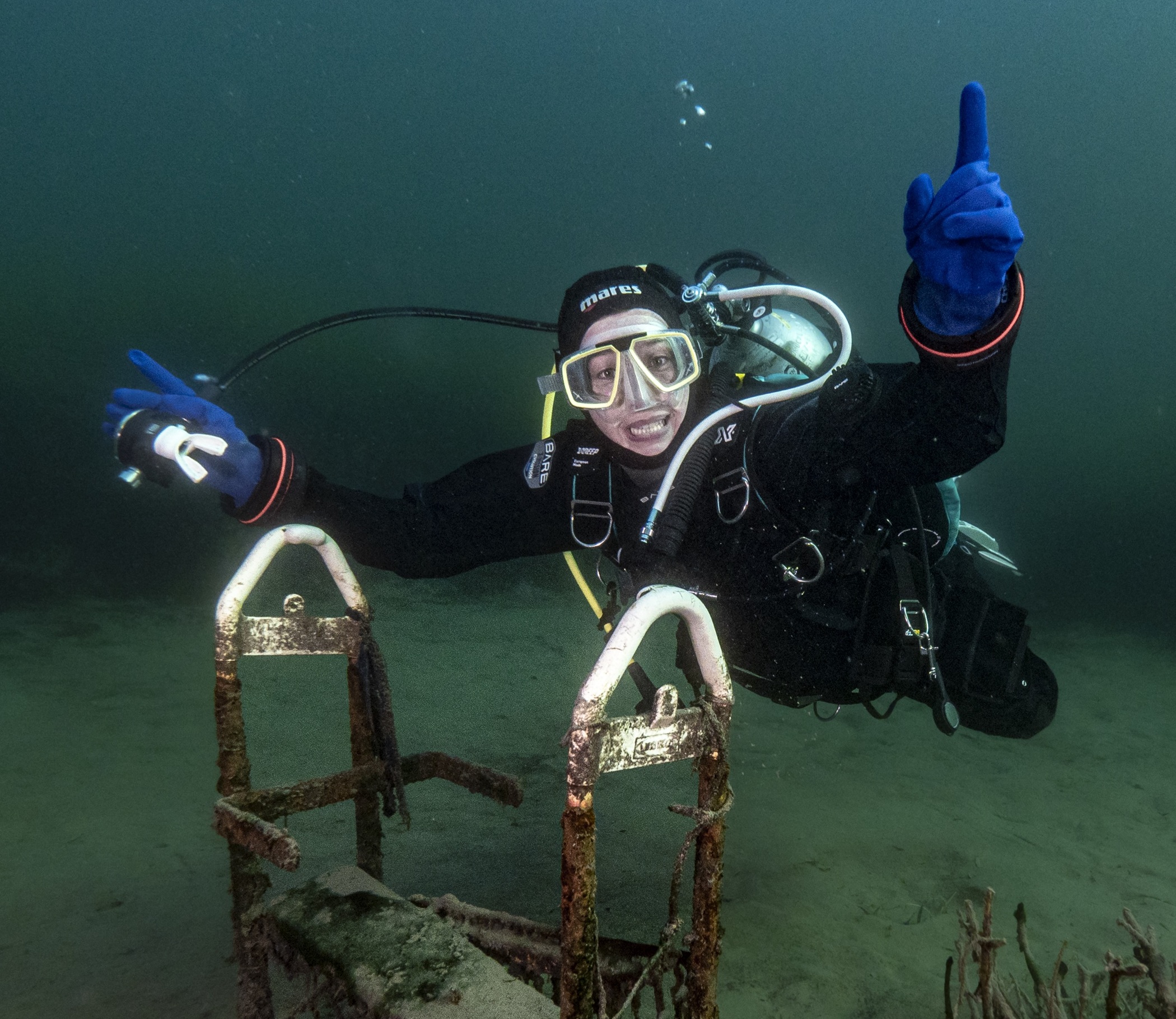 A smiling diver with arms extended hovering above some trash underwater