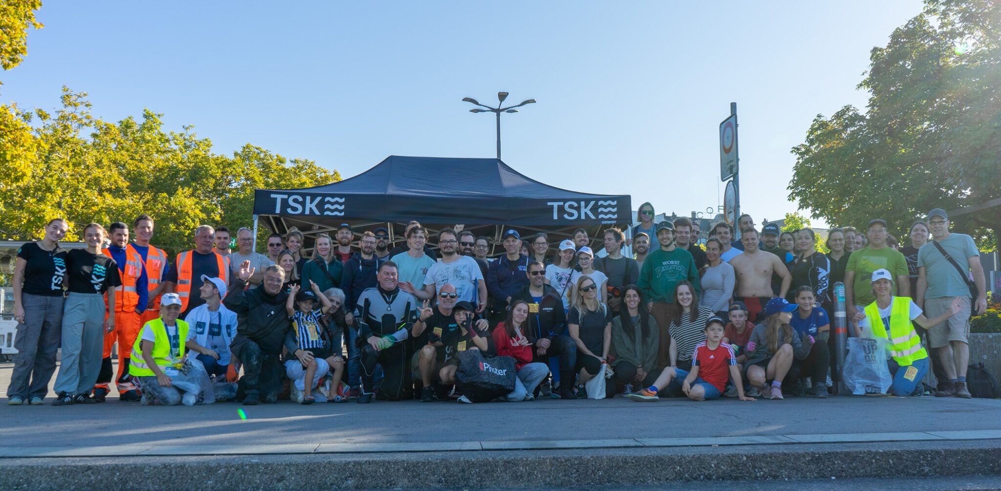 A group of at least 50 cleanup volunteers from TSK dive shop pose for a photo in front of a TSK pop up tent