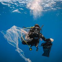 Diver holding a Dive Against Debris bag collecting plastic floating underwater