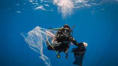 Diver holding a Dive Against Debris bag collecting plastic floating underwater