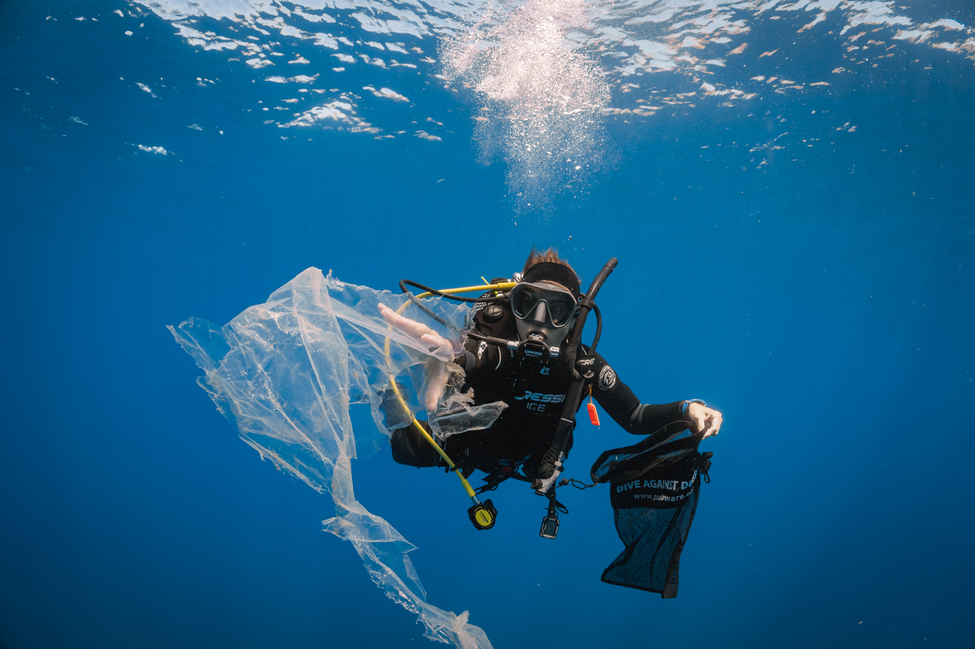 Diver holding a Dive Against Debris bag collecting plastic floating underwater