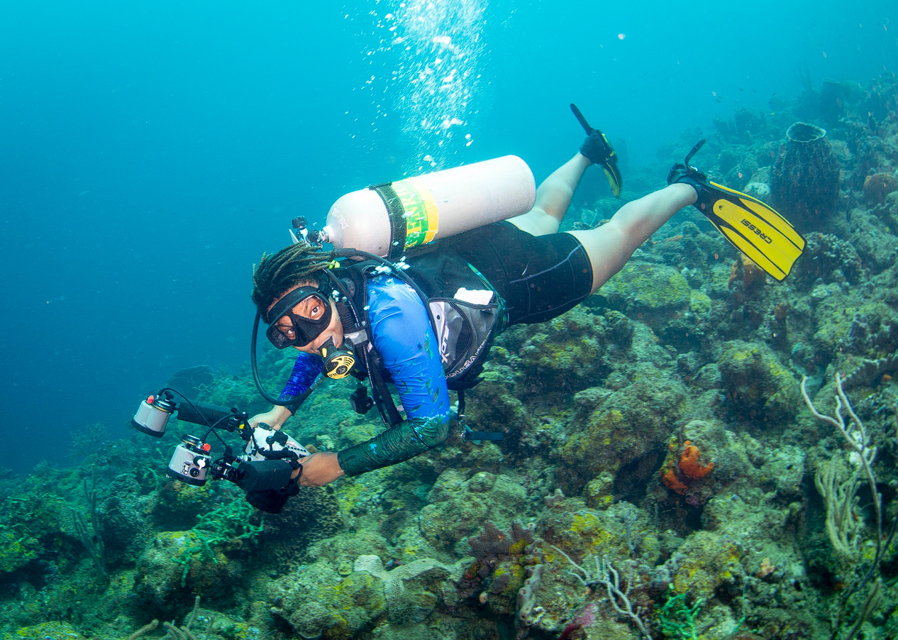 A diver holding an underwater camera swims over a reef in St. Lucia