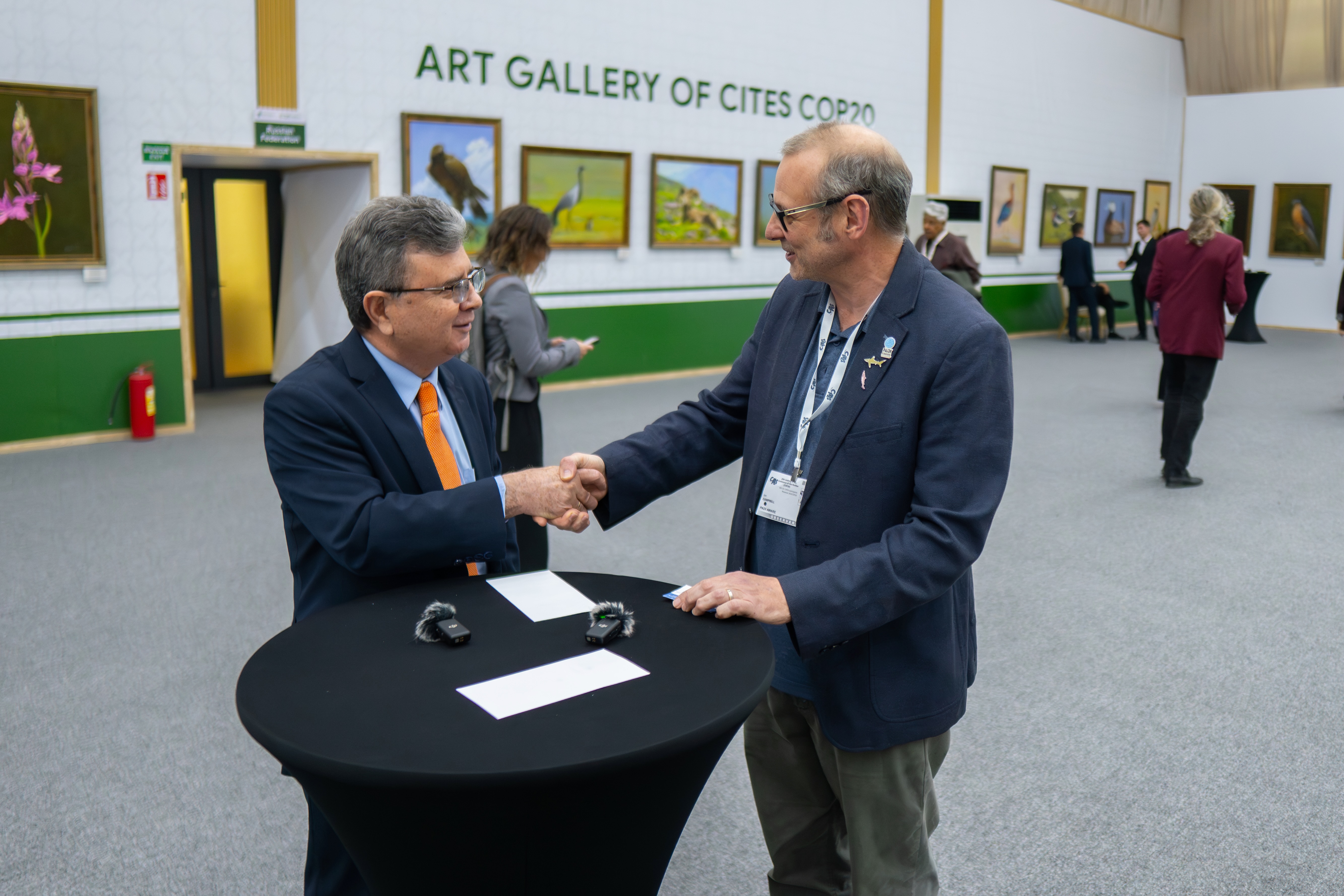 Twee mannen schudden elkaar de hand op de CITES COP20-top, voor de kunstgalerij van wilde dieren