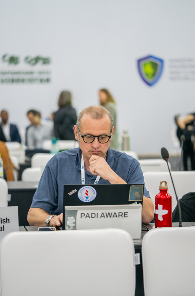 Ian Campbell van PADI AWARE zittend aan een bureau met een laptop tijdens een conferentie.  