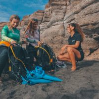 two divers set up their diving equipment on a beach in the Canary Islands with the assistance of a dive instructor