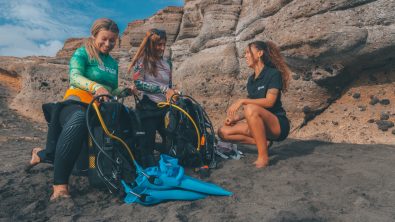 two divers set up their diving equipment on a beach in the Canary Islands with the assistance of a dive instructor