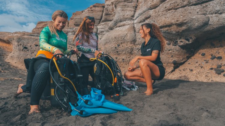 two divers set up their diving equipment on a beach in the Canary Islands with the assistance of a dive instructor