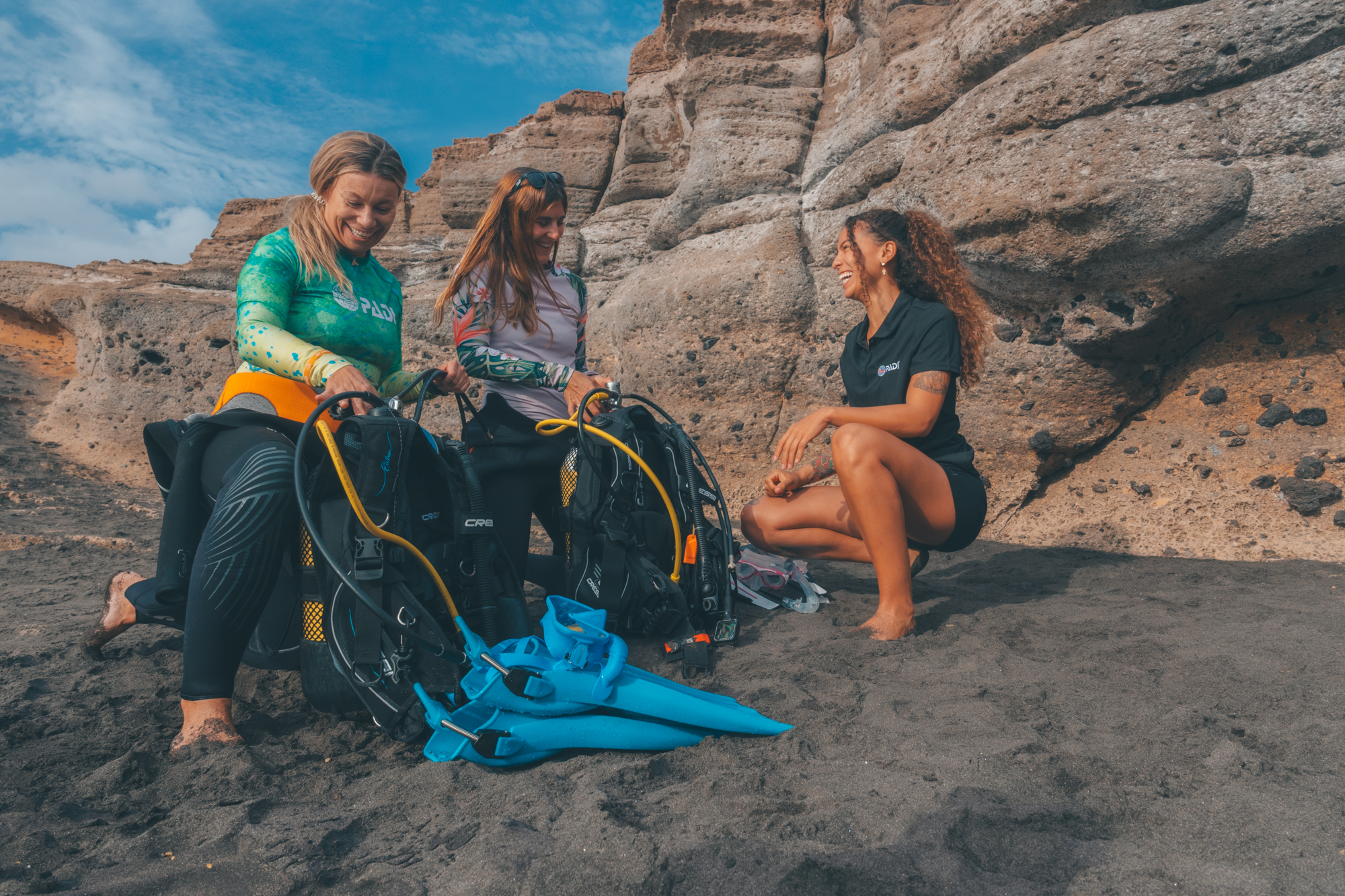 two divers set up their diving equipment on a beach in the Canary Islands with the assistance of a dive instructor
