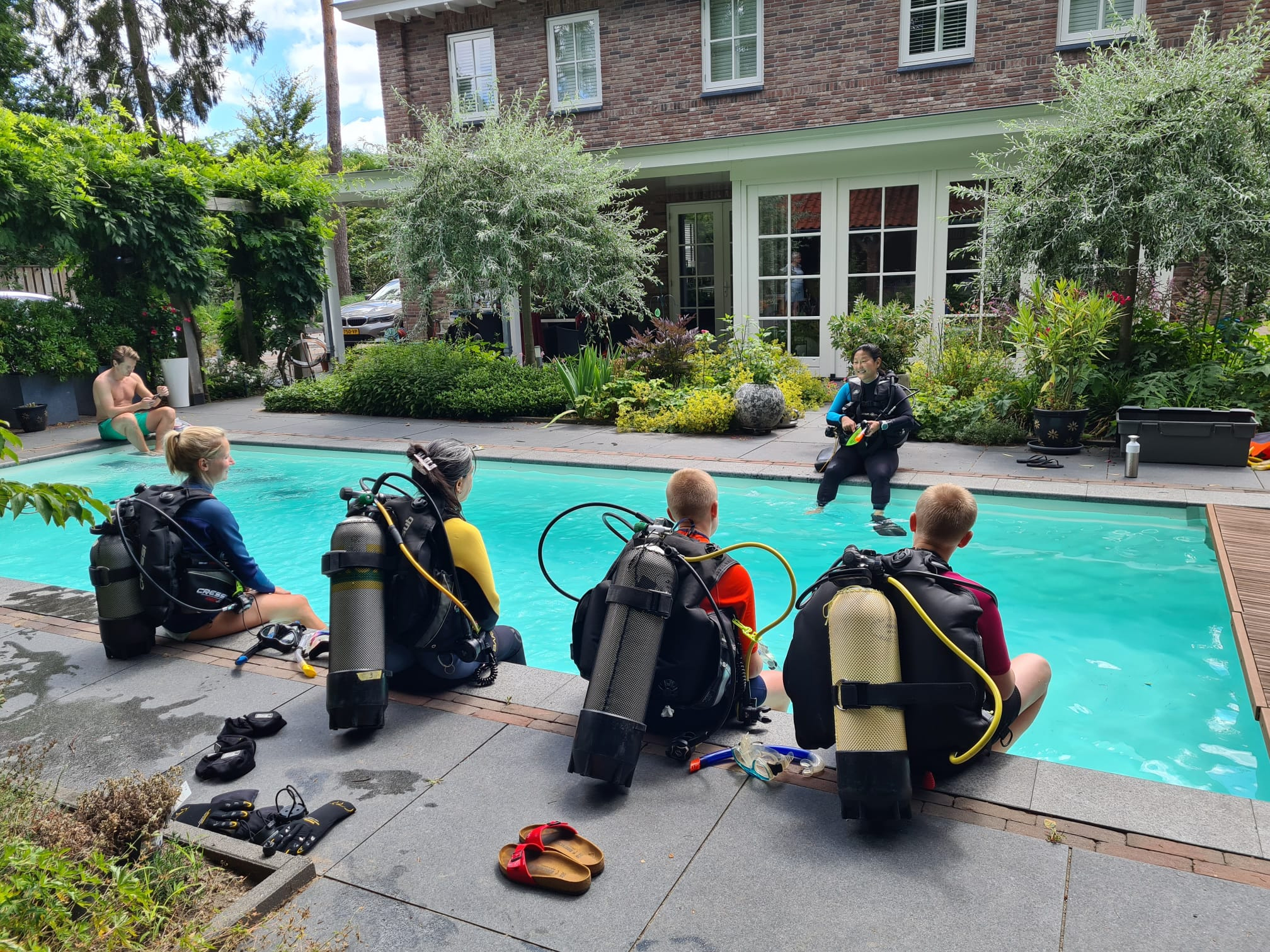 Four divers of the Wijnands family sitting on the side of a pool ready to dive in for confined water sessions