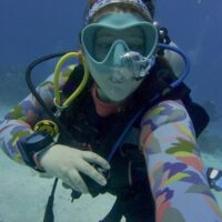 Sophie Negus taking a selfie underwater in a blue mask and colorful wetsuit