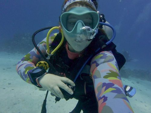 Sophie Negus taking a selfie underwater in a blue mask and colorful wetsuit