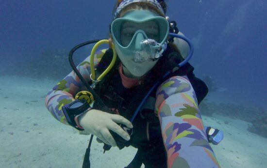Sophie Negus taking a selfie underwater in a blue mask and colorful wetsuit