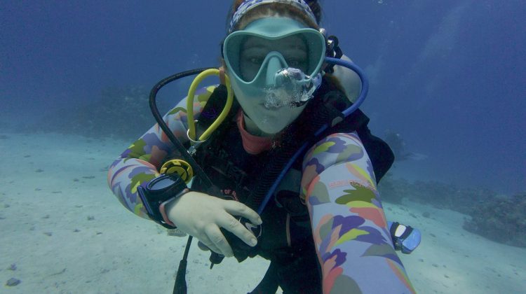 Sophie Negus taking a selfie underwater in a blue mask and colorful wetsuit