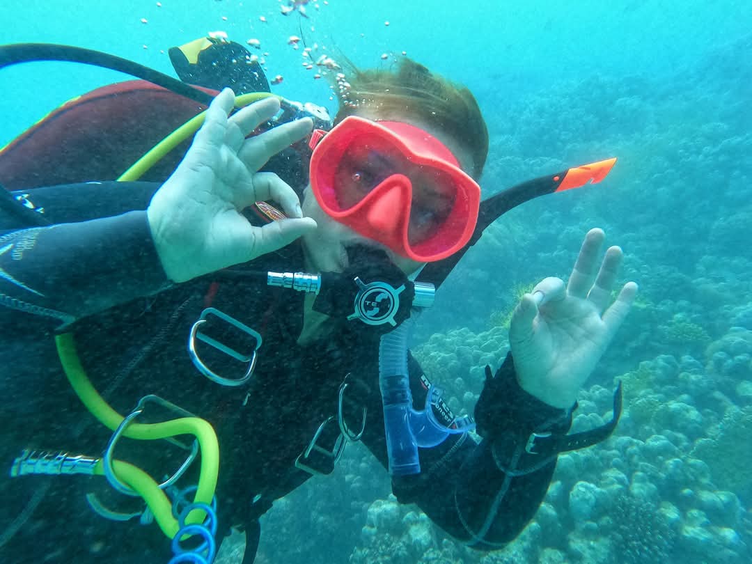 Close up of Elena Gushchina (lol2o) diving over a reef in a pink mask giving a double ok sign