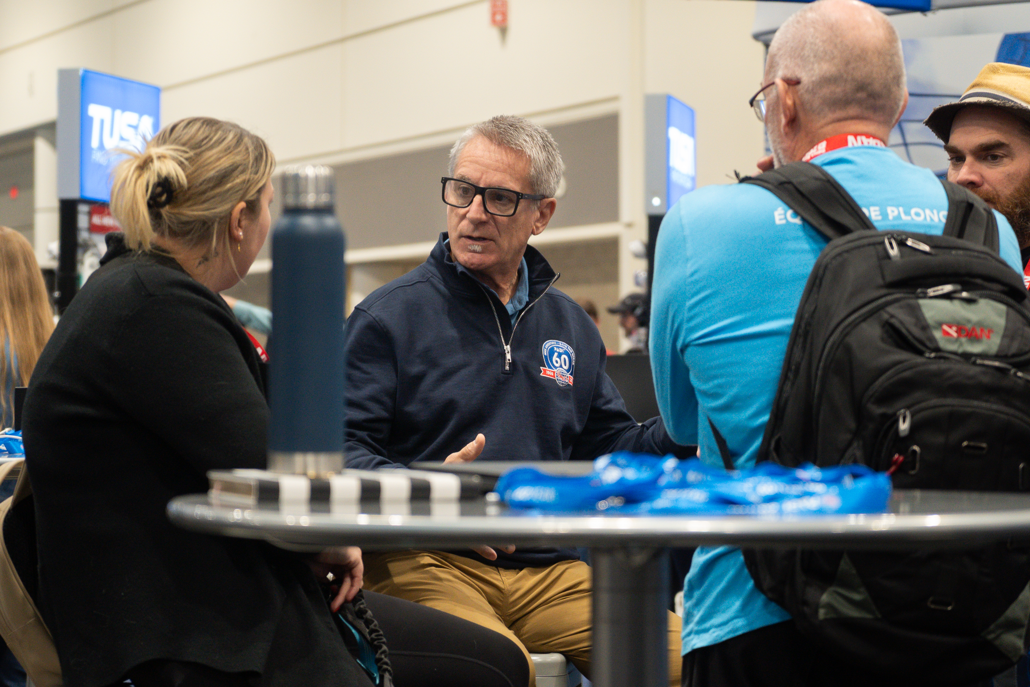 Three divers in PADI Gear talking at a table in a dive show