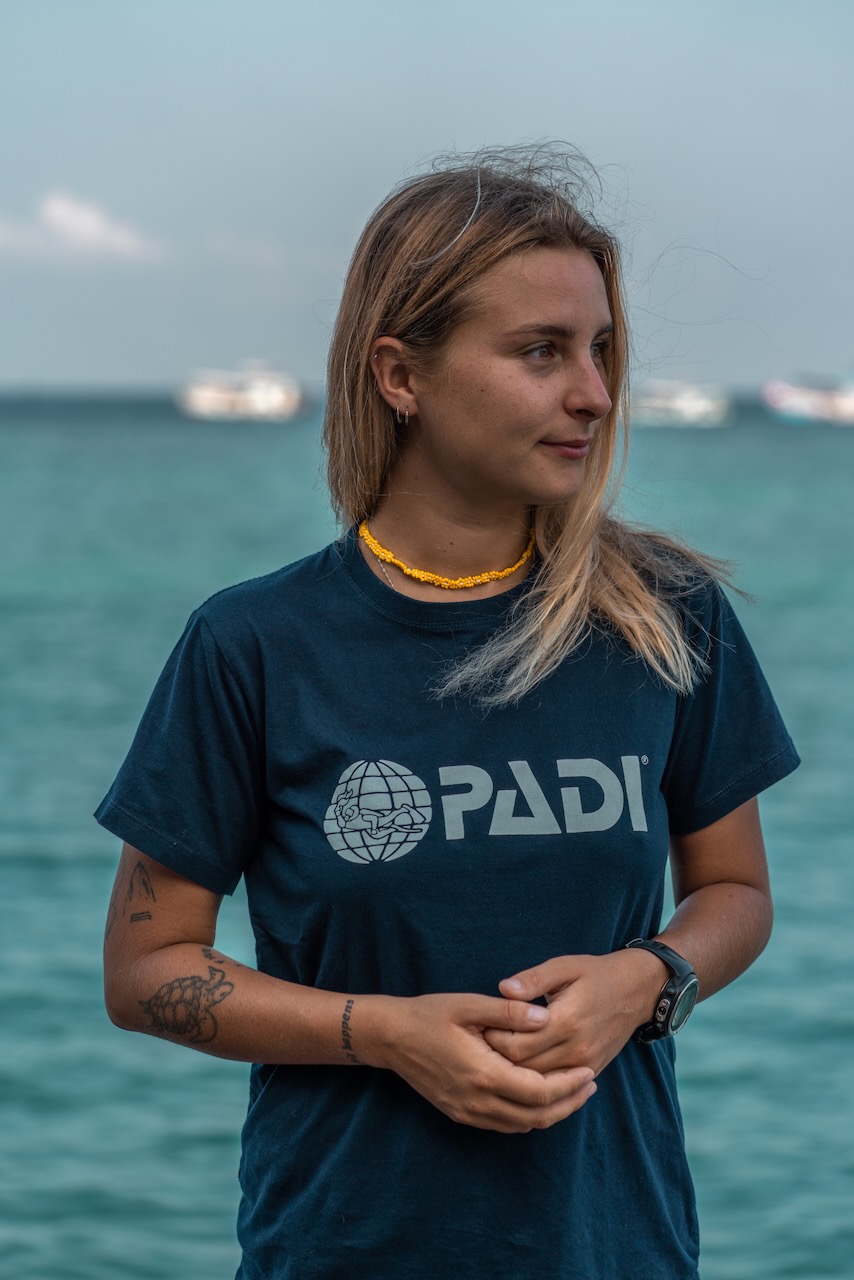 PADI AmbassaDiver 
Maëlly Faure de pie junto al mar con una camiseta PADI.