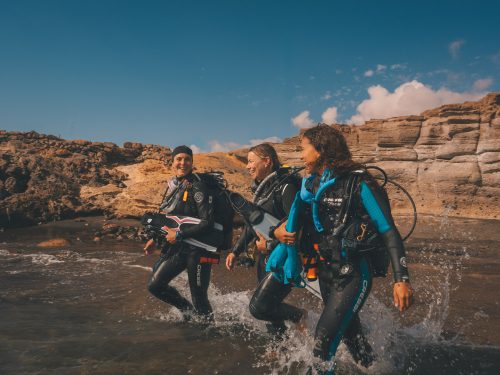 three divers walk int oth eocean together in Tenerife, Canary Islands, Spain