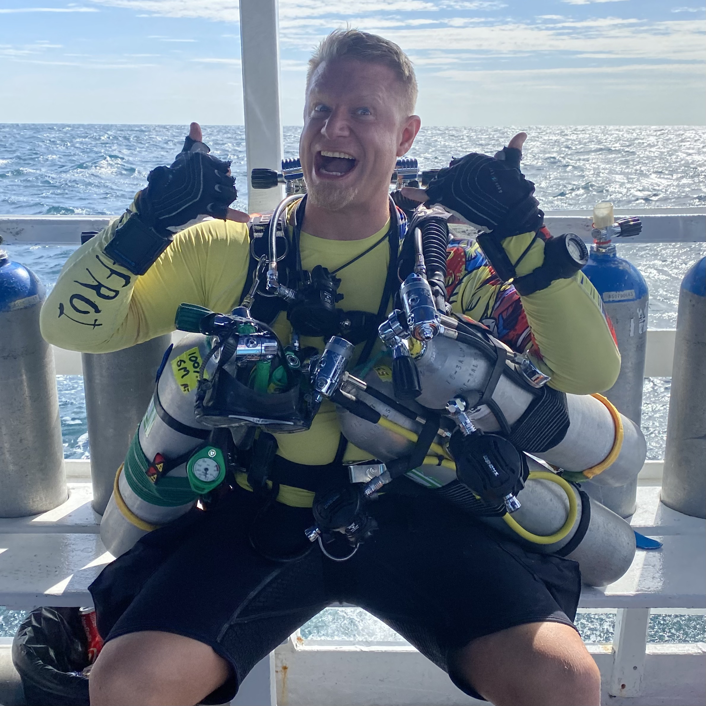 Photo of Peter Ryland Cairns sitting on a boat ready to go tec diving, with several tanks attached to him