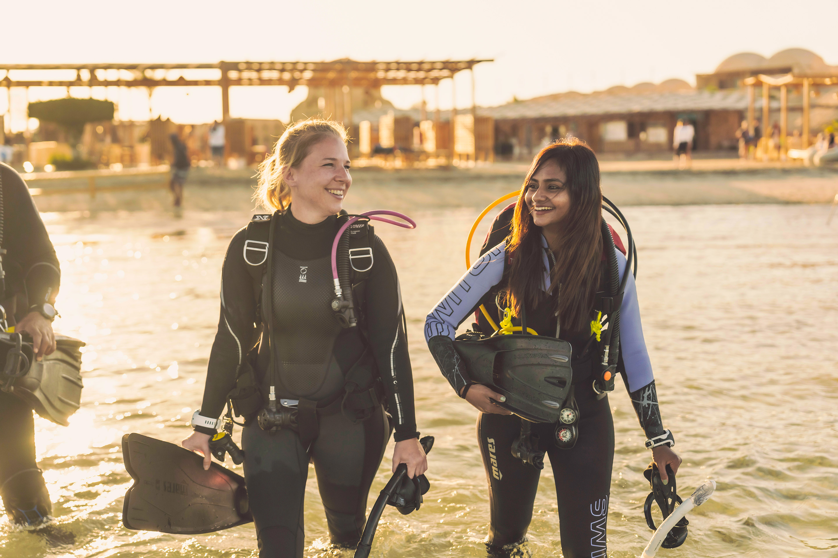 Two female divers walk into the water where scuba diving gear in Marsa Alam, Egypt. They are smiling at each other in anticipation of their dive.