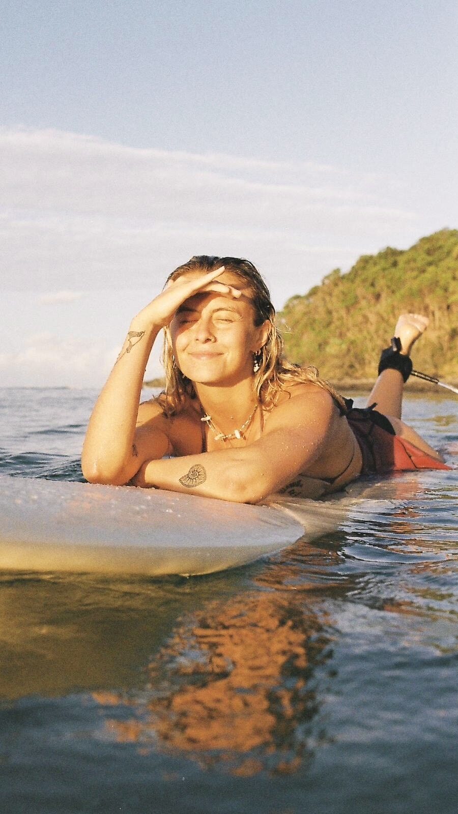 India Black smiles in the sun while floating on a surfboard.