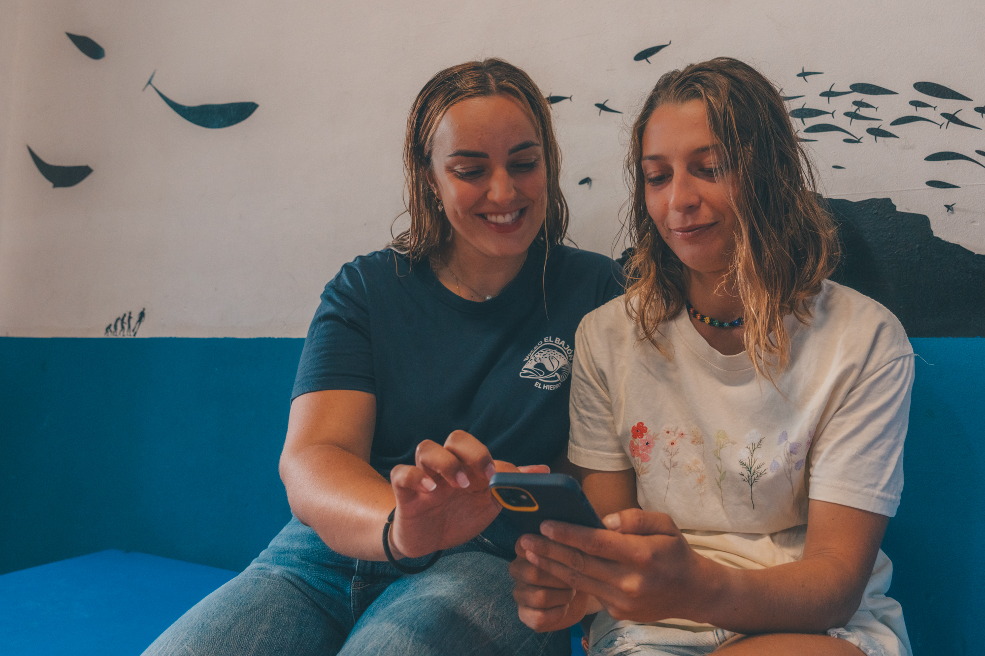 Two divers sitting on a blue couch logging data on a mobile phone