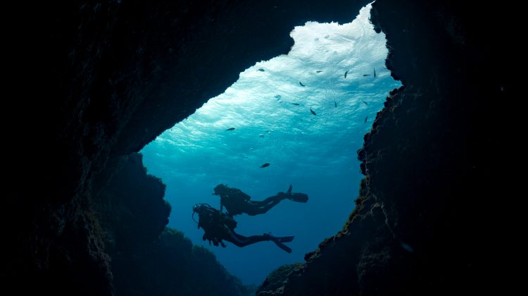 Silhouette of two divers seen through the opening of a cave