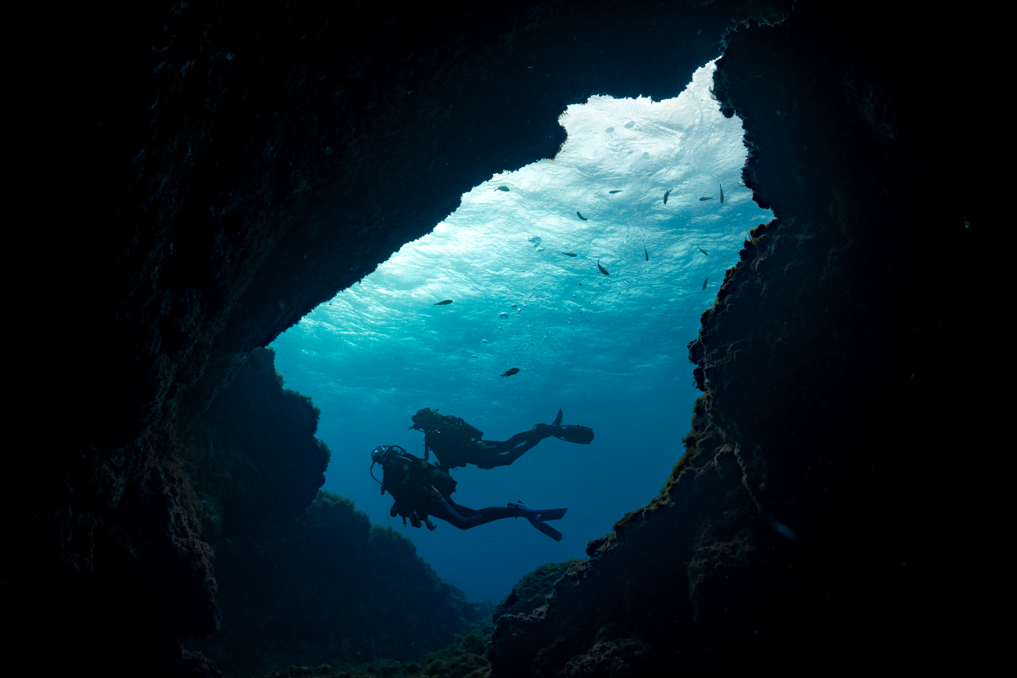 Silhouette of two divers seen through the opening of a cave