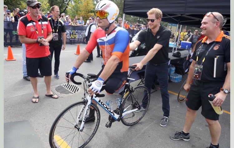 Invictus Games athlete Edwin de Wolf sits on a racing bike held by Prince Harry