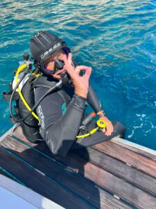 Divemaster and adaptive diver Edwin de Wolf gives the okay sign while sitting on the swim platform of a boat
